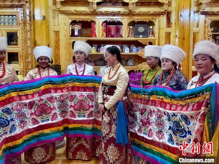 圖為女性展示村民自發(fā)繡制的“百米五彩哈達(dá)”?！±钣穹?攝